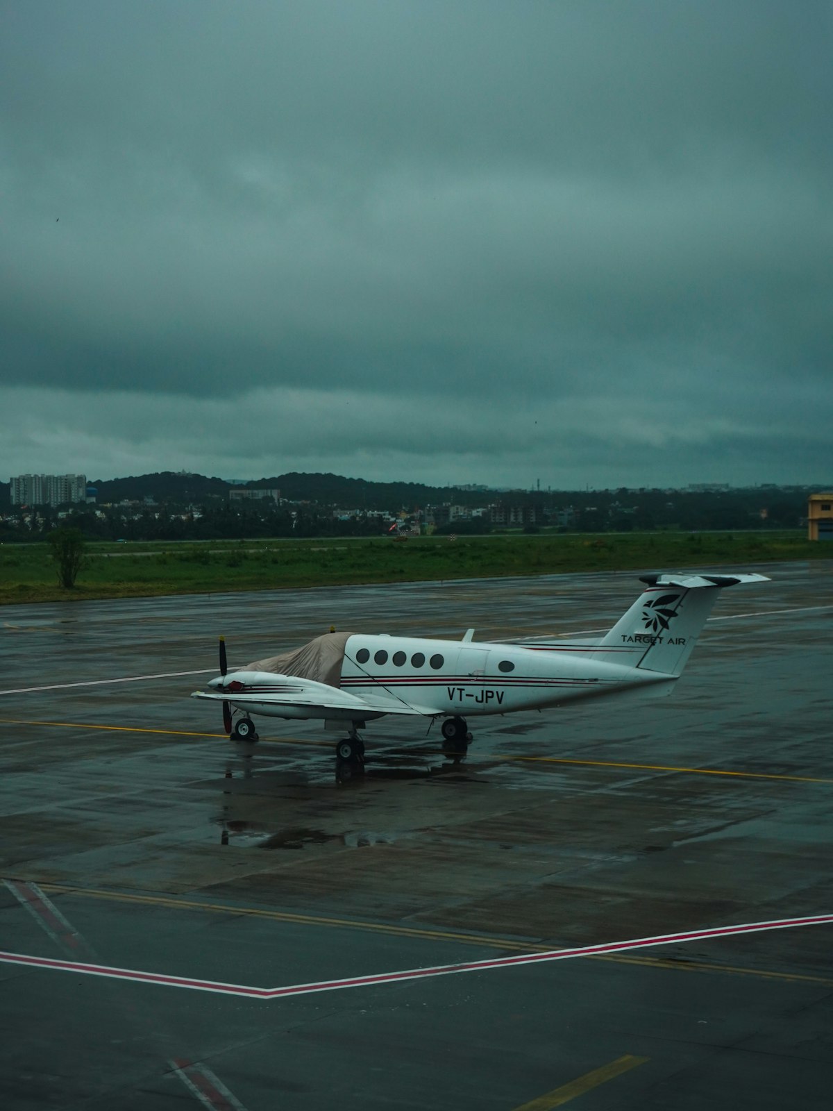 A small white aircraft parked on wet tarmac under an overcast sky